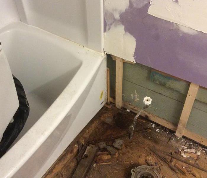 Stripped bathroom floor shows water damage at the corner of the tub