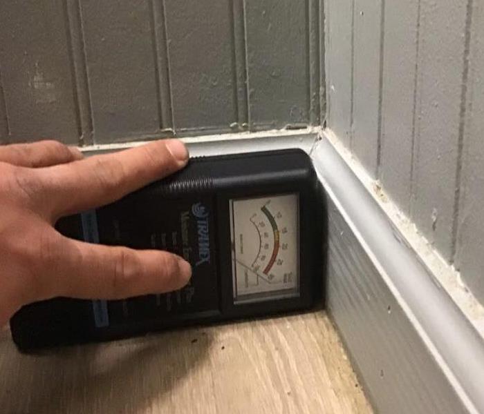 SERVPRO Technician holding a water meter reader against the baseboard checking for moisture