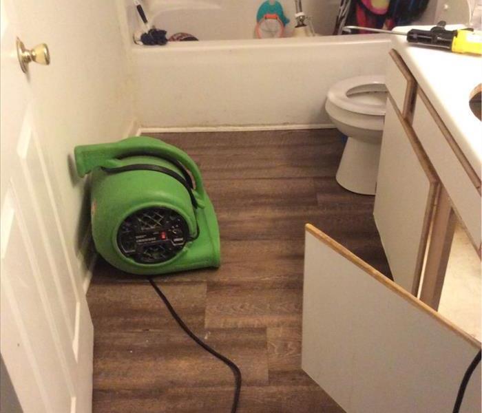 SERVPRO® green fan in bathroom where the pipe under the sink burst causing water damage