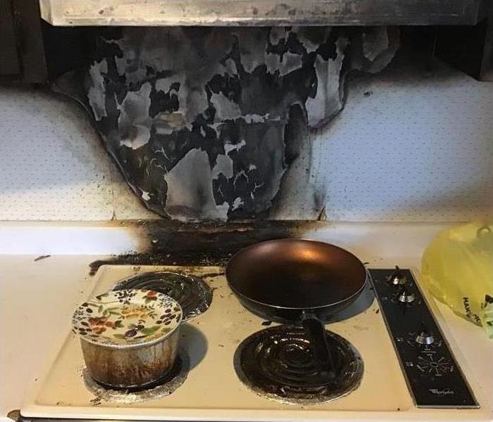 Stove with pans on it and the wall behind the stove is black from an unattended stove
